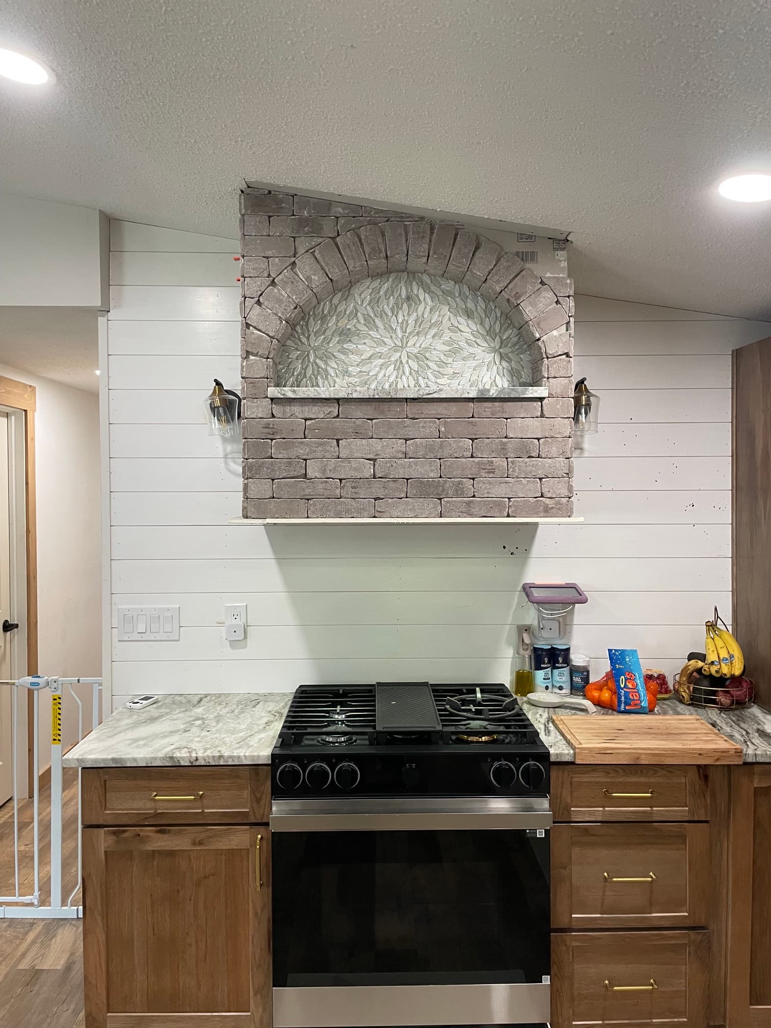 Modern kitchen featuring a brick arch with mosaic tile on a white shiplap wall.