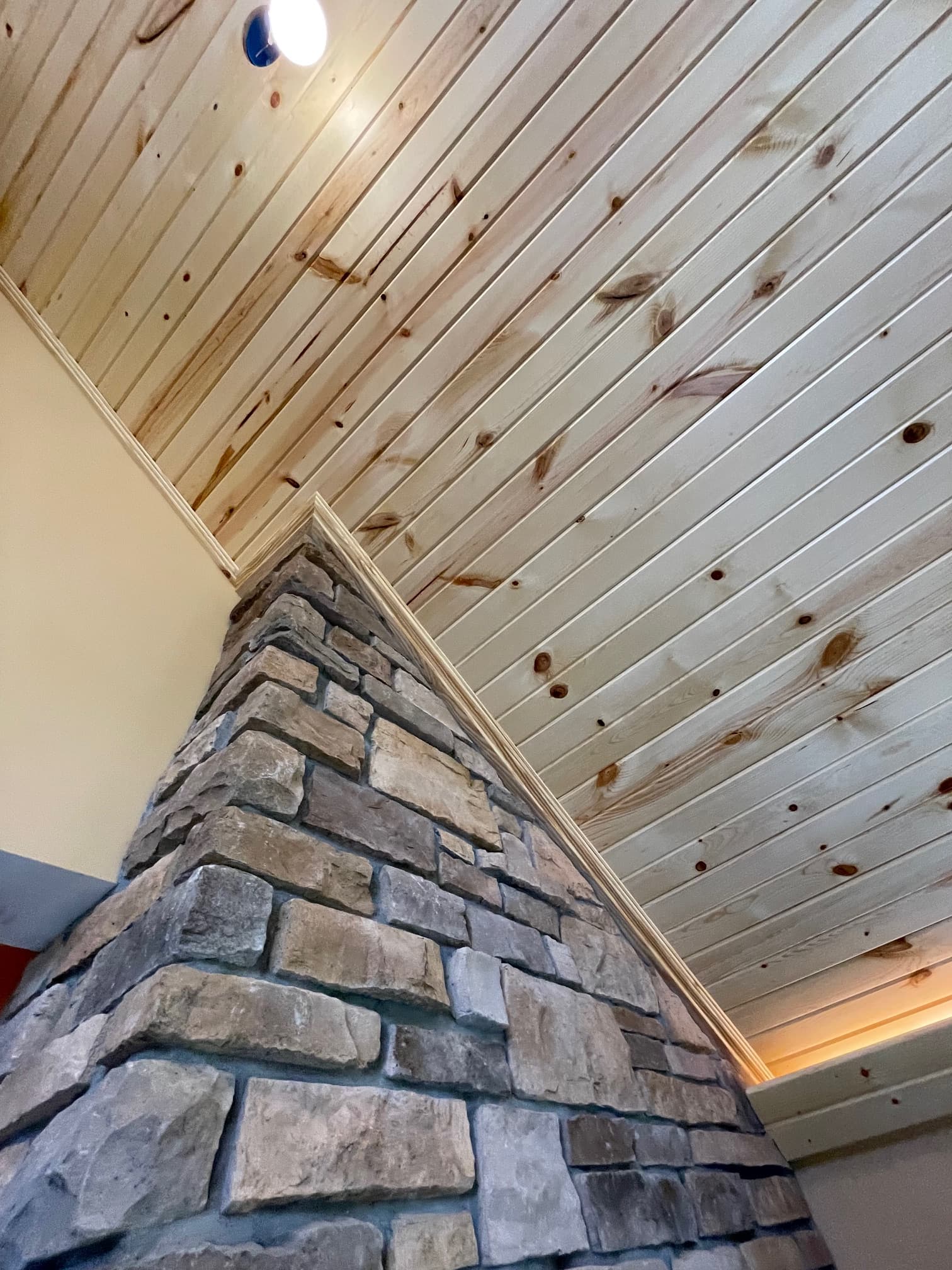 Low-angle view of a light wood plank ceiling meeting a textured grey stone pillar.