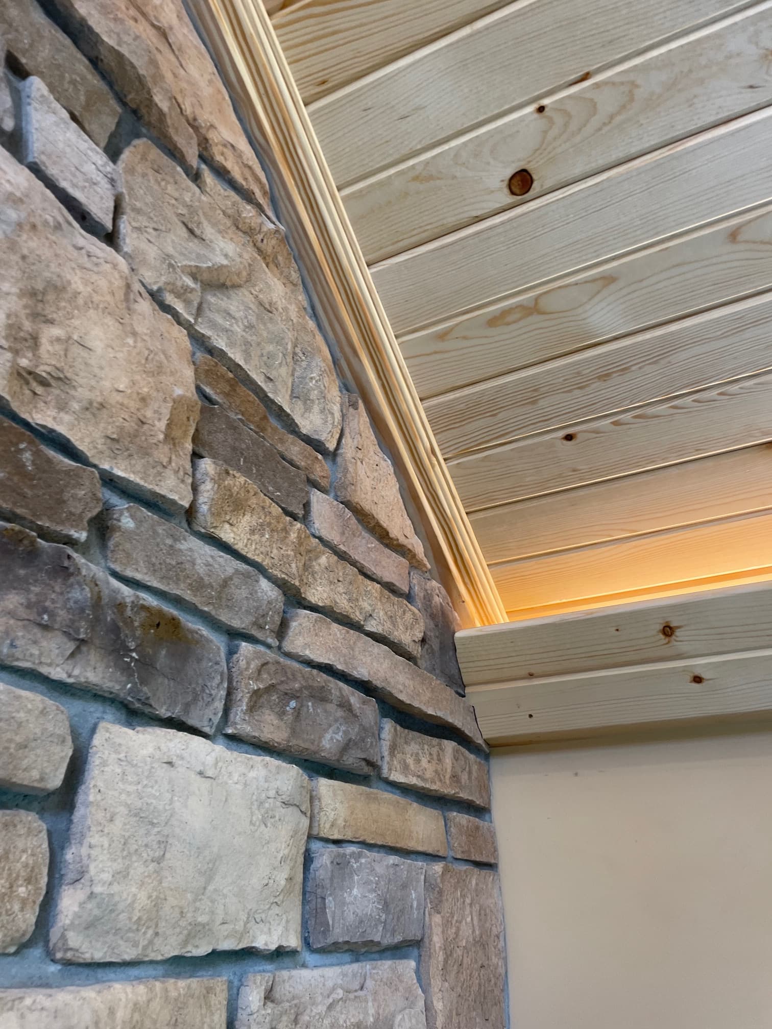 Textured stone floor meets light pine wood paneling with warm light glowing from a small gap.