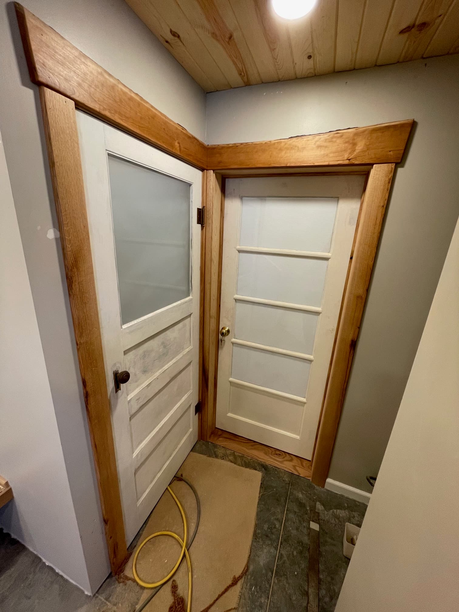 Two white doors with wooden trim meet at a right angle, creating a disorienting perspective.