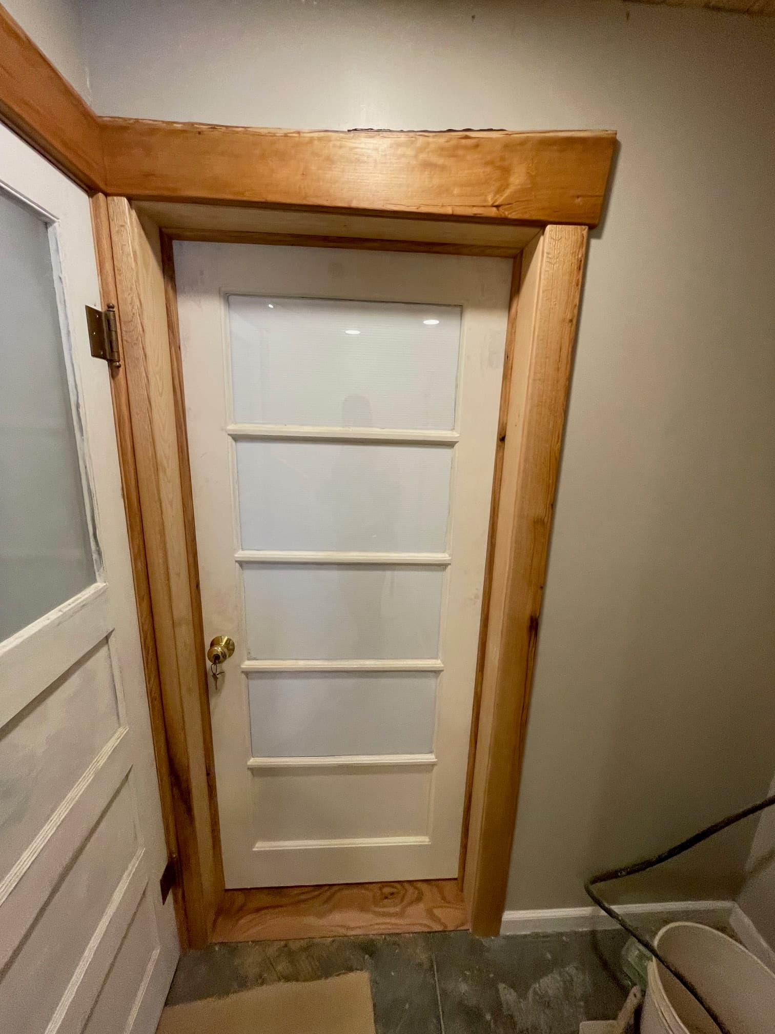 White door with glass panes and brass knob, encased in a thick, light-colored wooden frame.