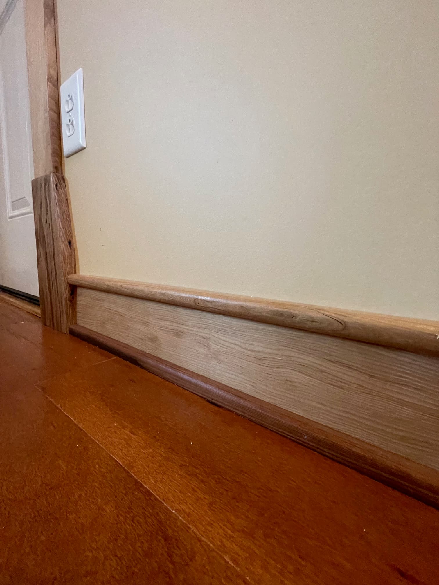 Cream wall with a white outlet, light wood trim, and a dark wood door.