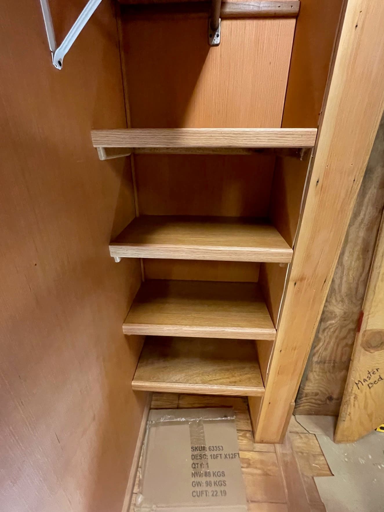 Narrow wooden closet featuring four built-in shelves and a cardboard box on the floor.