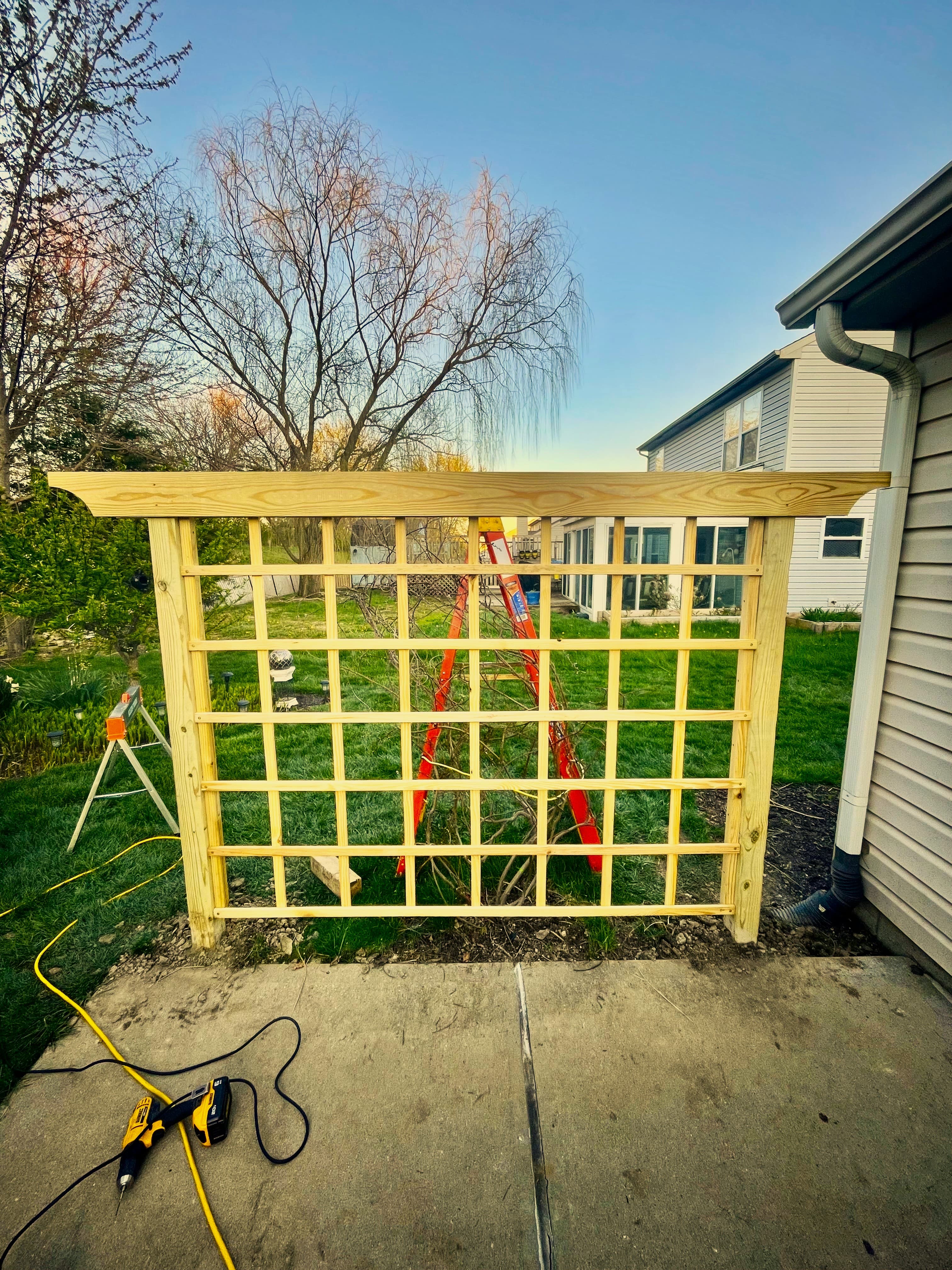 Newly built wooden garden trellis with a grid pattern standing on a backyard patio.